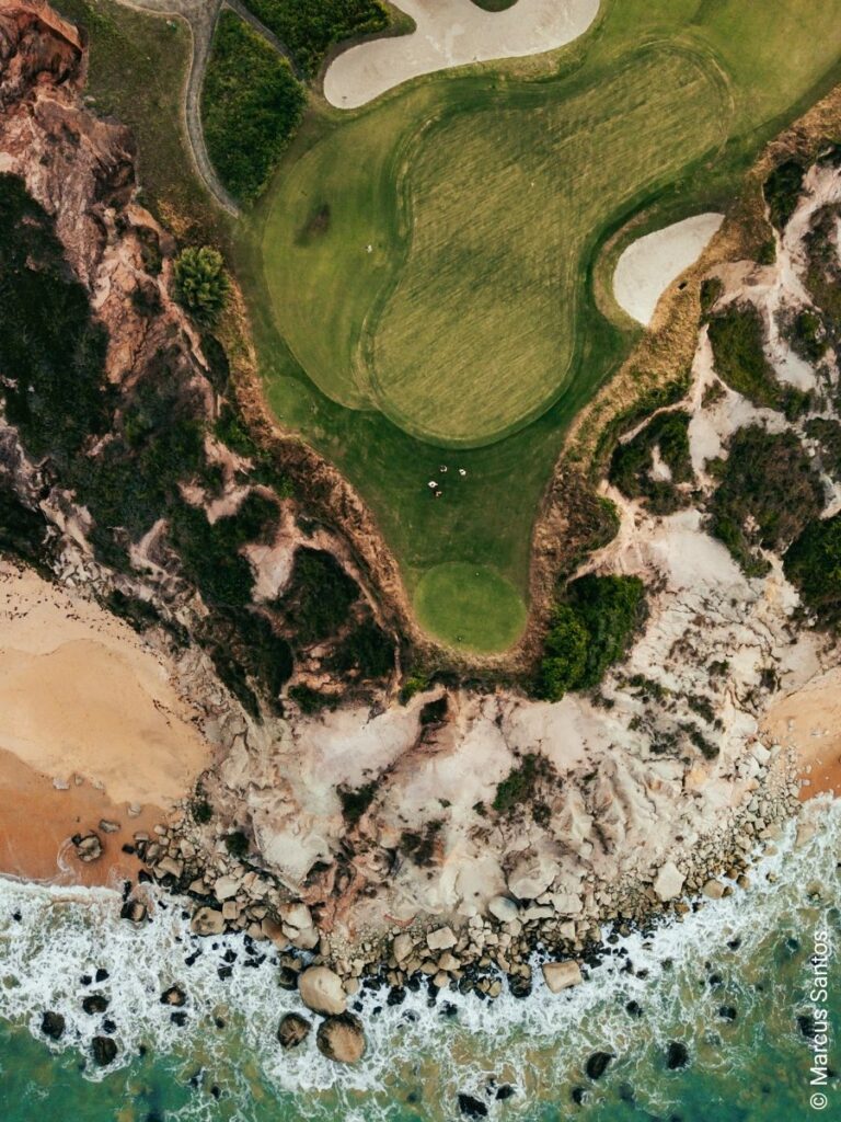 Luftaufnahme eines Golfplatzes an der Küste mit Felsen, Sandstrand und Meereswellen – exklusive Golfdestination für Golfreisen.